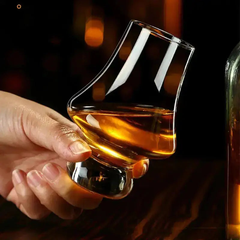 A hand holding a crystal tasting glass from Zendrop filled with whiskey, emphasizing the unique design and luxurious feel for enjoying fine beverages.